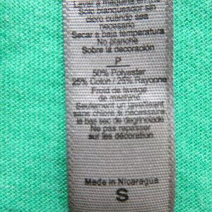 May include: A white care label with black text detailing the fabric composition and care instructions for a garment. The label reads "50% Polyester 25% Cotton/25% Rayon" and "Made in Nicaragua". The size "S" is also visible on the label.