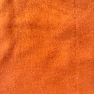 Puede incluir: Primer plano de una tela de color naranja brillante con una costura visible. La tela tiene un aspecto texturizado y tejido.
