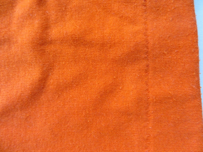 Puede incluir: Primer plano de una tela de color naranja brillante con una costura visible. La tela tiene un aspecto texturizado y tejido.