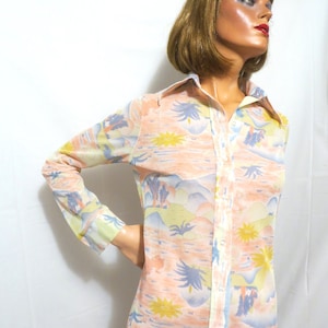 Puede incluir: Una camisa de manga larga con botones, de fondo rosa pastel y estampado tropical colorido. El estampado presenta palmeras, flores y un paisaje azul y verde.