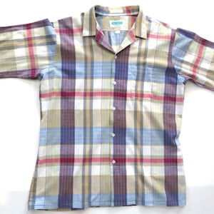 May include: A long-sleeved button-down shirt with a plaid pattern in shades of blue, red, yellow, and white. The shirt has a collar and a pocket on the left side.