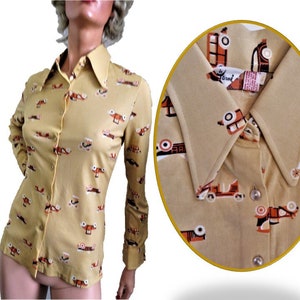 May include: A yellow long-sleeved button-down shirt with a pattern of small red, orange, and black cars. The shirt has a pointed collar and a button closure. The label reads "Carvel".