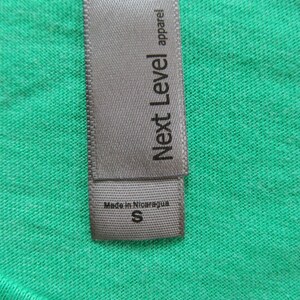May include: A grey clothing label with the text "Next Level apparel" and "Made in Nicaragua" with a size "S" printed on it.