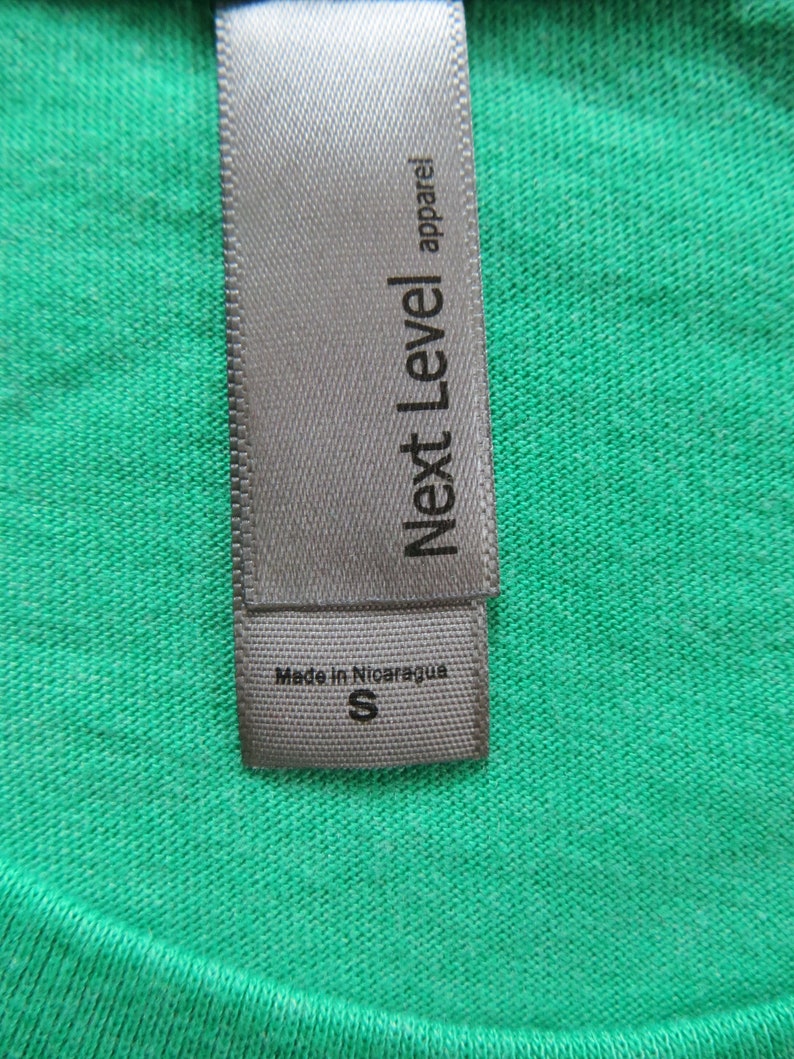 May include: A grey clothing label with the text "Next Level apparel" and "Made in Nicaragua" with a size "S" printed on it.
