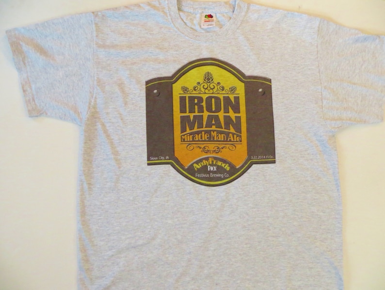 May include: Gray t-shirt with a brown and yellow label that says "Iron Man Miracle Man Ale" and "Andy Franks Festbier Brewing Co."