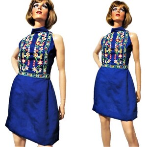 May include: A sleeveless blue dress with a high neckline and a floral embroidered design. The dress has a fitted bodice and a slightly flared skirt.