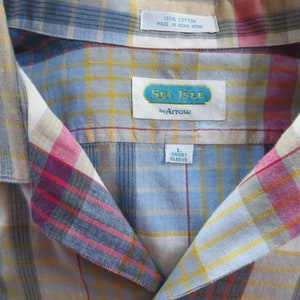 May include: A blue, yellow, red, and white plaid short-sleeve shirt with a Sea Isle by Arrow label. The shirt is labeled size L.