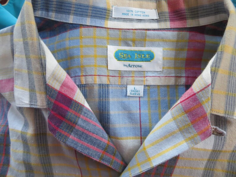 May include: A blue, yellow, red, and white plaid short-sleeve shirt with a Sea Isle by Arrow label. The shirt is labeled size L.