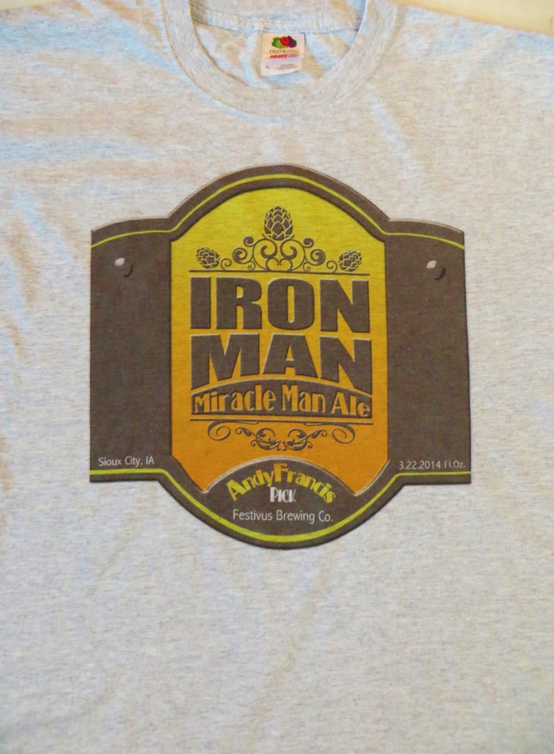 May include: A gray t-shirt with a brown and yellow label that says "Iron Man Miracle Man Ale" with the text "Andy Francis Pick Festivus Brewing Co." and "Sioux City, IA 3.22.2014 FL.OZ."