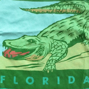 May include: A green t-shirt featuring a graphic of an alligator with the word "FLORIDA" printed beneath it.