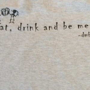 May include: A white t-shirt with black text that reads "eat, drink and be merry" with a small drawing of a person below the text and the words "dmb" written above the person.