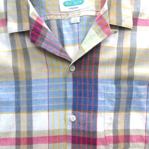 May include: A blue, yellow, red, and white plaid button-down shirt with a Sea Isle by Arrow label. The shirt has a button-up front and a pocket on the left side.
