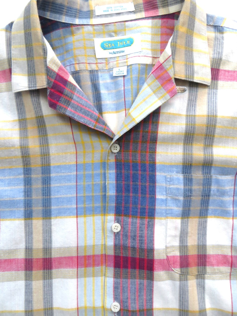 May include: A blue, yellow, red, and white plaid button-down shirt with a Sea Isle by Arrow label. The shirt has a button-up front and a pocket on the left side.