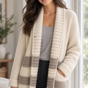 May include: A cream-colored open-front cardigan featuring a thick ribbed shawl collar, long sleeves with folded cuffs, and two front pockets. The garment is decorated with horizontal stripes in a muted taupe color across the lower section.