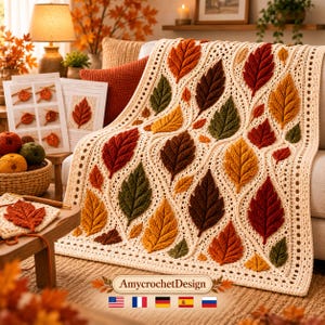 May include: A cream-colored crochet blanket featuring a textured pattern of three-dimensional autumn leaves in shades of red, orange, brown, and green. The leaves are arranged in a flowing, vine-like design across the surface of the blanket.