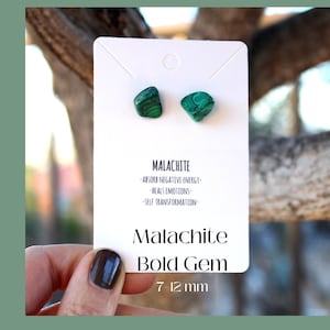 May include: A pair of green malachite gemstone earrings on a white card. The card says "Malachite Bold Gem 7-12 mm" and lists the properties of malachite: "Absorb Negative Energy, Heals Emotions, Self Transformation."
