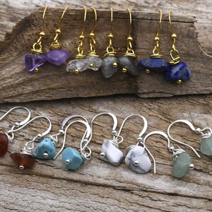 Puede incluir: Dos filas de pendientes con diferentes piedras preciosas de colores. La fila superior presenta pendientes de oro con piedras de amatista, cuarzo transparente, labradorita y lapislázuli. La fila inferior presenta pendientes de plata con piedras de cornalina, turquesa, howlite y aventurina verde.