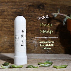 Könnte beinhalten: Weißer Aromatherapie-Inhalator aus Kunststoff mit einem Etikett mit der Aufschrift "ORGANIC Deep Sleep Aromatherapy Essential Oil Inhaler". Der Inhalator liegt auf einer Holzoberfläche mit verstreuten grünen Blättern.