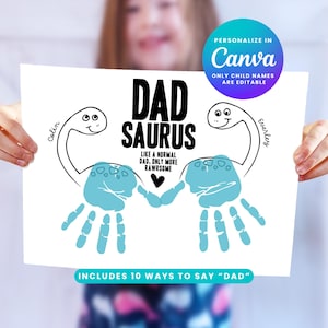 May include: A white print featuring the text "DAD SAURUS" in black, with a dinosaur illustration and handprint art in light blue. The print includes the names "Colin" and "Everley". The text "INCLUDES 10 WAYS TO SAY 'DAD'" is also present.