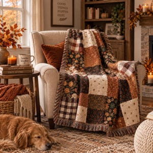 May include: A patchwork throw blanket featuring a variety of autumn-themed patterns including brown and white buffalo check, floral prints, and solid rust-coloured squares. The blanket has a fringed edge and is draped over a beige upholstered armchair.