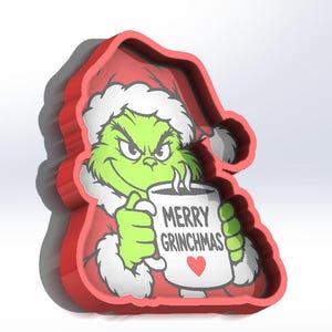 May include: A red plastic cookie cutter shaped like a character wearing a Santa hat and holding a white mug. The mug features the text MERRY GRINCHMAS and a small red heart. The character has green skin, a mischievous expression, and white fur trim.