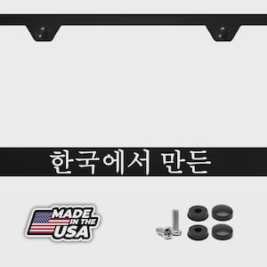 May include: A black rectangular license plate frame featuring white Korean text at the bottom. The set includes two metal screws and four black plastic screw covers, along with a sticker displaying the American flag and the text Made in the USA.