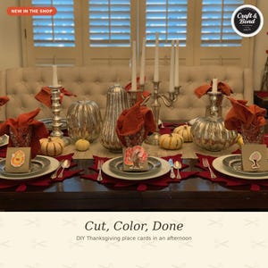 May include: A Thanksgiving table setting featuring white plates, red leaf-shaped placemats, and orange napkins. The centerpiece includes silver pumpkins, a tall silver candelabra with white candles, and small paper place cards with tree illustrations.