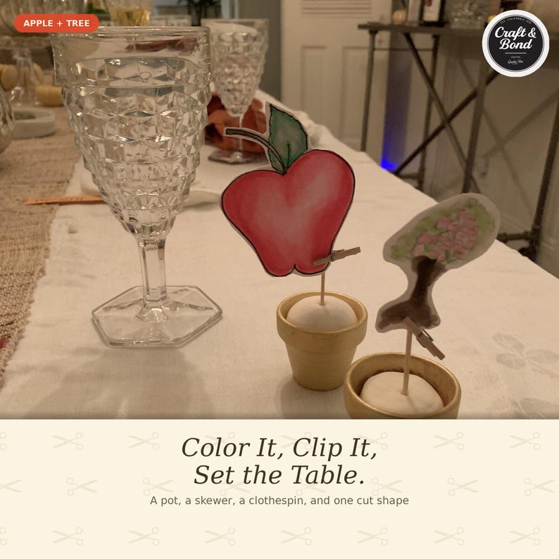 May include: Two small beige pots each containing a white spherical base, a wooden skewer, and a miniature wooden clothespin. One clothespin holds a red apple cutout with a green leaf, and the other holds a cutout of a tree with pink blossoms.