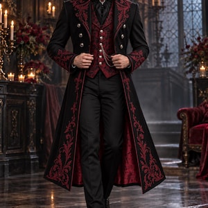 Op de afbeelding: Een lange zwarte jas met rood bloemenborduursel, voorzien van een hoge kraag, zilveren knopen en een bijpassend rood vest met patroon en een zilveren ketting. Het ensemble bevat een zwarte broek en een zwart overhemd met een donkerrode broche.