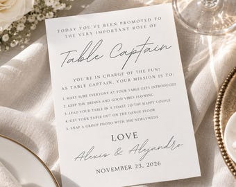 May include: A white rectangular wedding card with black text that reads: Today you've been promoted to the very important role of Table Captain. You're in charge of the fun! As Table Captain, your mission is to: 1. Make sure everyone at your table gets introduced, 2. Keep the drinks and good vibes flowing, 3. Lead your table in a toast to the happy couple, 4. Get your table out on the dance floor, 5. Snap a group photo with the newlyweds. Love, Alexis & Alejandro, November 23, 2026.