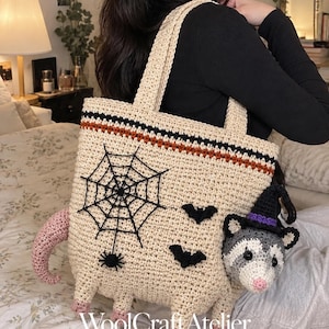 May include: A beige crochet tote bag featuring a black spider web, a small spider, and two black bats. A three-dimensional crochet opossum head wearing a purple and black witch hat is attached to the side. The bag has a pink tail and feet, with the text WoolCraftAtelier Crochet Pattern Design Studio printed at the bottom.