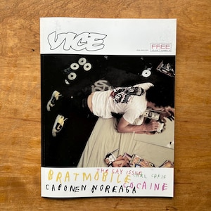 Könnte beinhalten: Eine Ausgabe des Vice-Magazins mit einem Titelbild, das eine Person zeigt, die auf einem Bett mit verstreuten CDs und Geld liegt. Der Text auf dem Cover umfasst "VICE", "FREE", "THE GAY ISSUE", "BRATMOBILE", "CARL CRAIG", "CAPONEN NOREAGA" und "COCAINE".