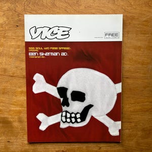 Könnte beinhalten: Eine Ausgabe des Vice-Magazins mit weißer Kopfzeile und dunkelrotem Cover, das eine große weiße Totenkopf-Grafik mit gekreuzten Knochen zeigt. Der Text lautet Vice, Free, Volume 7 Number 9, SSS Soul Two Page Spread, Droors, Ben Sherman Ad, Transfer Ad.