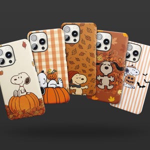 May include: Five smartphone cases featuring Snoopy in various autumn-themed designs. The cases display patterns of pumpkins, falling leaves, plaid, and stripes in shades of orange, brown, and cream, with illustrations of the character Snoopy.