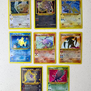 May include: A collection of eight Shining Pokémon trading cards arranged in three rows. The cards feature illustrations of Noctowl, Steelix, Raichu, Magikarp, Charizard, Kabutops, Tyranitar, and Celebi, each with unique text and game statistics.