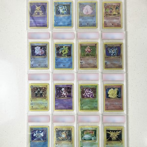Può includere: Una collezione di sedici carte collezionabili vintage disposte in una griglia quattro per quattro, ciascuna racchiusa singolarmente in una custodia protettiva in plastica trasparente. Le carte mostrano varie creature illustrate con testo.