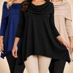 May include: A long-sleeve tunic top featuring a draped cowl neckline and a textured fabric finish. The garment has a flared, asymmetrical hemline and is presented in three distinct colors: navy blue, solid black, and a light beige neutral tone.