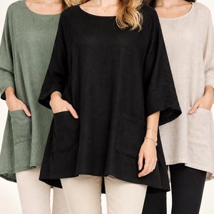 May include: A loose-fitting tunic top with three-quarter length sleeves and two front patch pockets, available in solid black, olive green, and beige. The garment features a wide round neckline and a slightly longer hemline at the back.