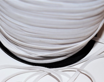 May include: A spool of white elastic cord, with a length of cord unwound and lying on a white surface.