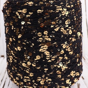 May include: A spool of black yarn with gold sequins woven throughout. The yarn is wound tightly and the sequins are visible on all sides.