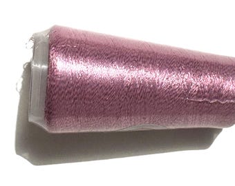 May include: A spool of shimmering, dusty rose-colored thread. The thread is tightly wound on a white plastic core and wrapped in clear plastic. The thread has a metallic sheen, reflecting light.