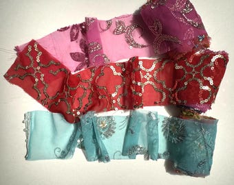 May include: A collection of colorful fabric ribbons with intricate sequin and bead embellishments. The ribbons are in shades of pink, red, and teal, with detailed floral and geometric patterns. The fabric appears to be sheer and delicate.