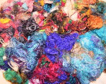 May include: A close-up of a pile of colorful, textured yarn scraps. The yarn is a mix of different colors, including blue, green, purple, red, and orange. The yarn is arranged in a random pattern, creating a visually appealing and textured surface.