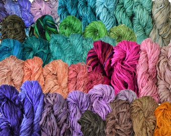 May include: A collection of colorful, hand-dyed silk ribbon yarn. The yarn is arranged in rows, with each row featuring a different color. The colors include teal, purple, pink, orange, brown, and green.