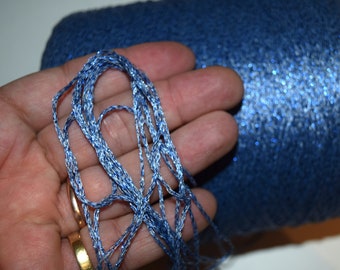 May include: A skein of blue and silver yarn with a sparkly finish. The yarn is held in a hand, showing the texture and sheen of the thread.