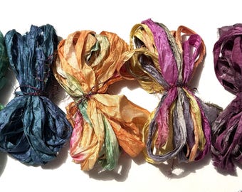 May include: Five bundles of colorful silk ribbon in shades of green, blue, orange, pink, and purple. Each bundle is tied with a dark thread. The ribbons have a textured, crinkled appearance, suggesting they are made of silk.
