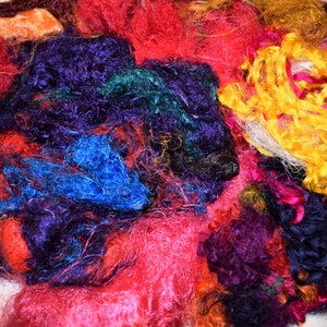 Op de afbeelding: Een stapel kleurrijke zijdevezels in tinten rood, roze, paars, blauw, groen, geel en oranje. De vezels zijn zacht en pluizig en perfect voor knutselen of kunstprojecten.