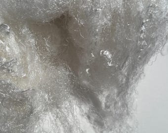 May include: Close-up of a pile of white, fluffy fiber material. The fibers are densely packed and appear soft, with a slightly translucent quality. The texture is fine and wispy, suggesting a lightweight textile or filling material.
