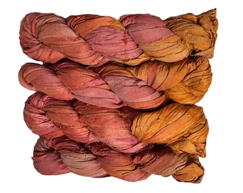 May include: Braided silk ribbon in shades of rose, rust, and gold. The ribbon is tightly woven and appears to be made of multiple strands. The texture is slightly wrinkled, and the colors blend together in a gradient.