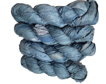 May include: A skein of hand-dyed, textured yarn in shades of blue. The yarn appears to be made of fabric strips, tightly twisted and braided together. The color variations create a visually interesting and unique craft supply.
